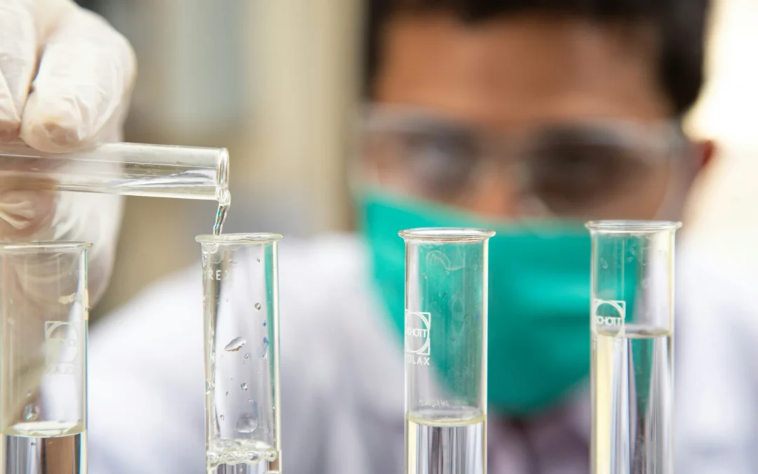 Naukowc w masce wlewający płyn do probówek w laboratorium chemicznym.